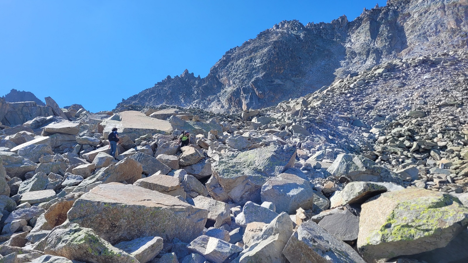 Photo de Faustin et Charline qui avancent au milieu d'énirmes rochers ; on voit le sommet du Pic d'Ardiden derrière eux.
