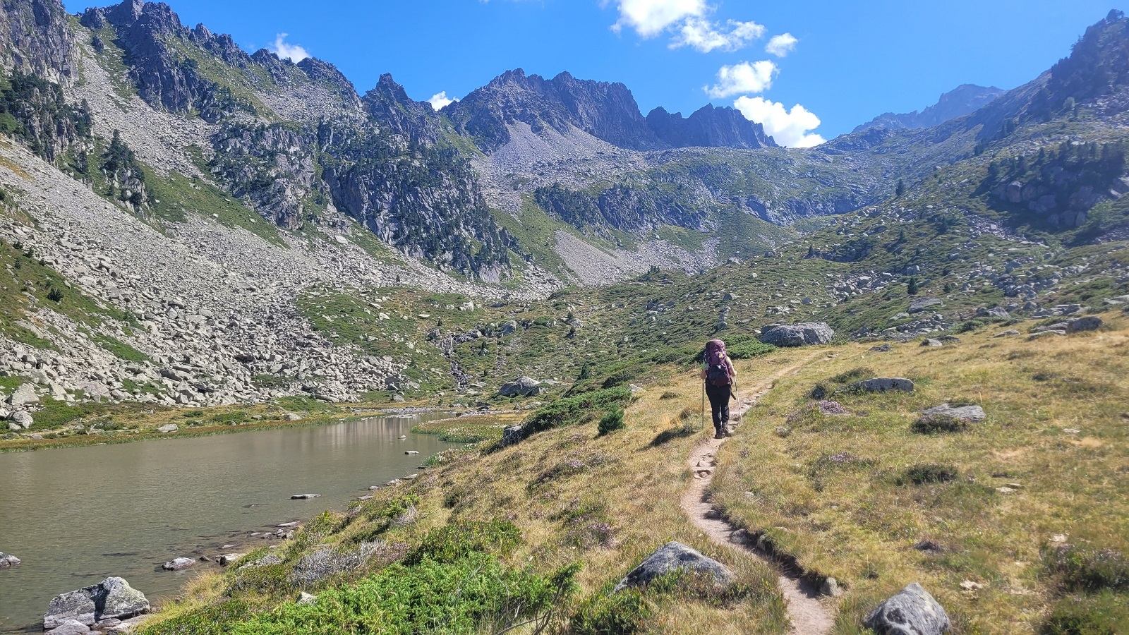 Photo de Charline avançant sur un sentier avec un lac à sa gauche et une crête déchirée les surplombant.